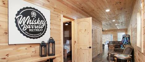 Interior de una cabaña de madera con un letrero que indica Whiskey Barrel Retreat, una mesa de comedor y una zona de estar acogedora.