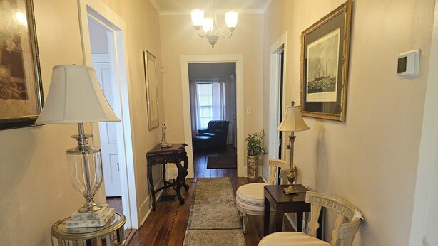 A hallway with a chandelier, a framed picture, a lamp, a small table with a giraffe figurine, and a chair.