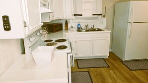 A compact kitchen with white cabinets, a stove, a microwave, a sink, and a refrigerator.