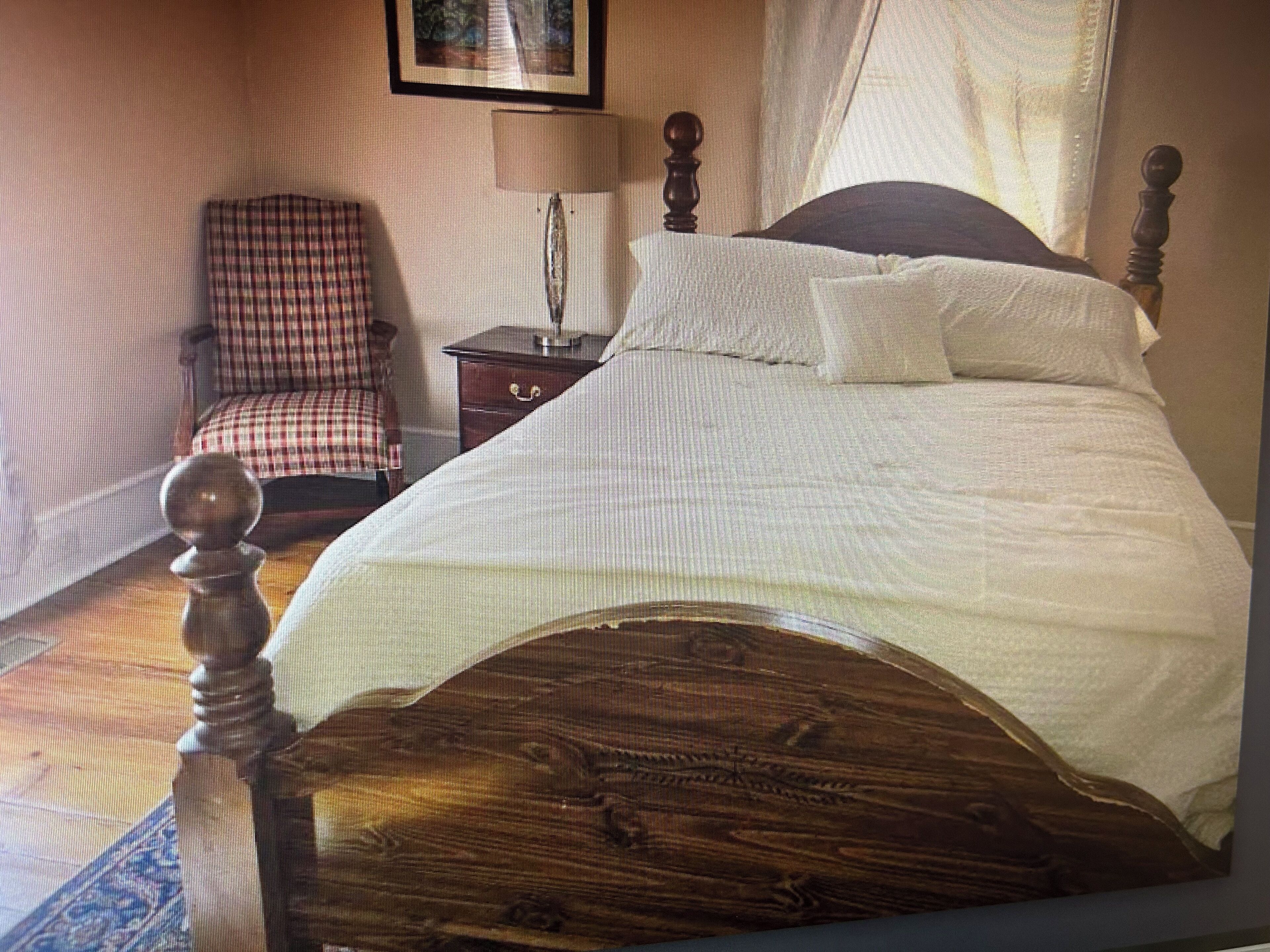 Un dormitorio con cama de madera, una silla, una mesita de noche y una lámpara.