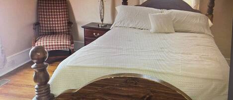 Un dormitorio con cama de madera, una silla, una mesita de noche y una lámpara.