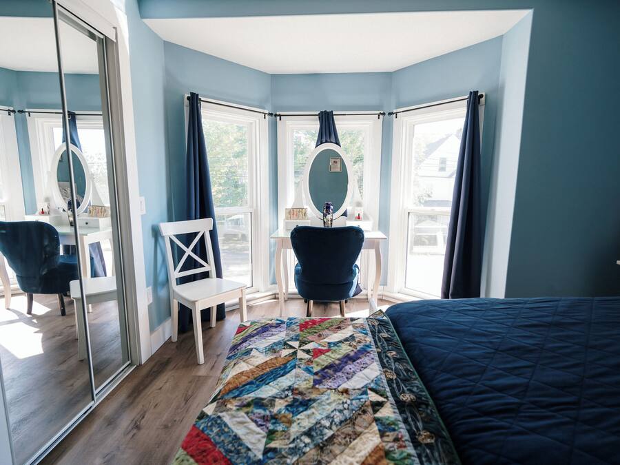 Un dormitorio con una cama grande, un escritorio con silla, un espejo y vistas al exterior.