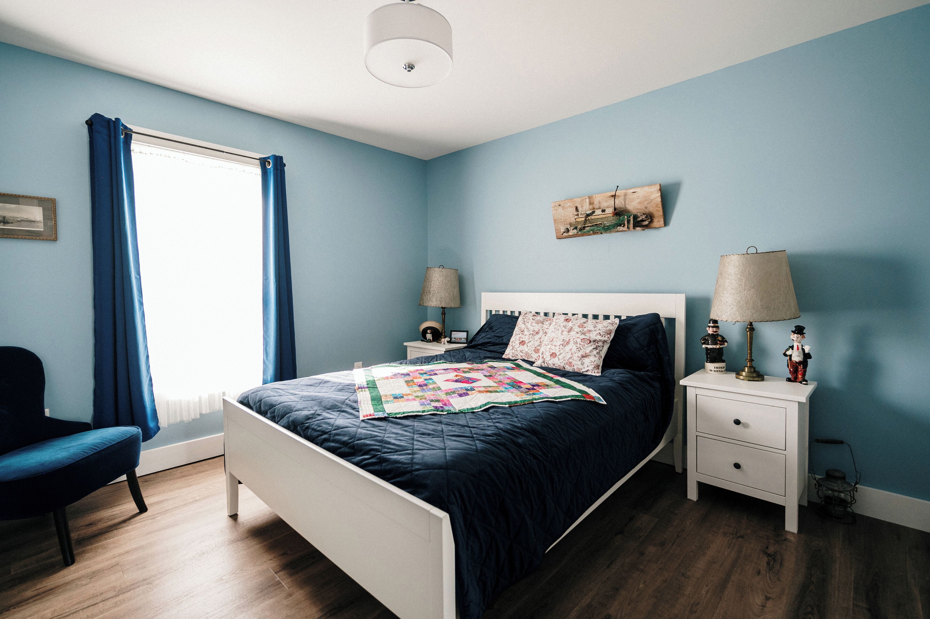 Une chambre à coucher avec un lit, des tables de chevet, une chaise et une fenêtre avec des rideaux.