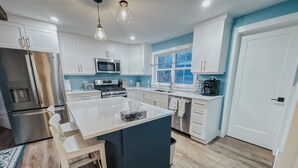 A modern kitchen with white cabinets, stainless steel appliances, a central island, and a window providing natural light. - The Granville Affair (Bridgetown)