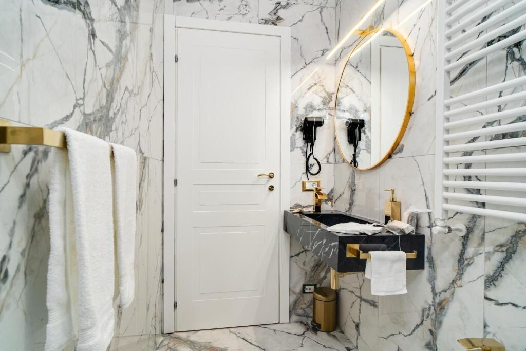A bathroom with a marble wall, a white door, a sink with gold fixtures, and a towel rack.