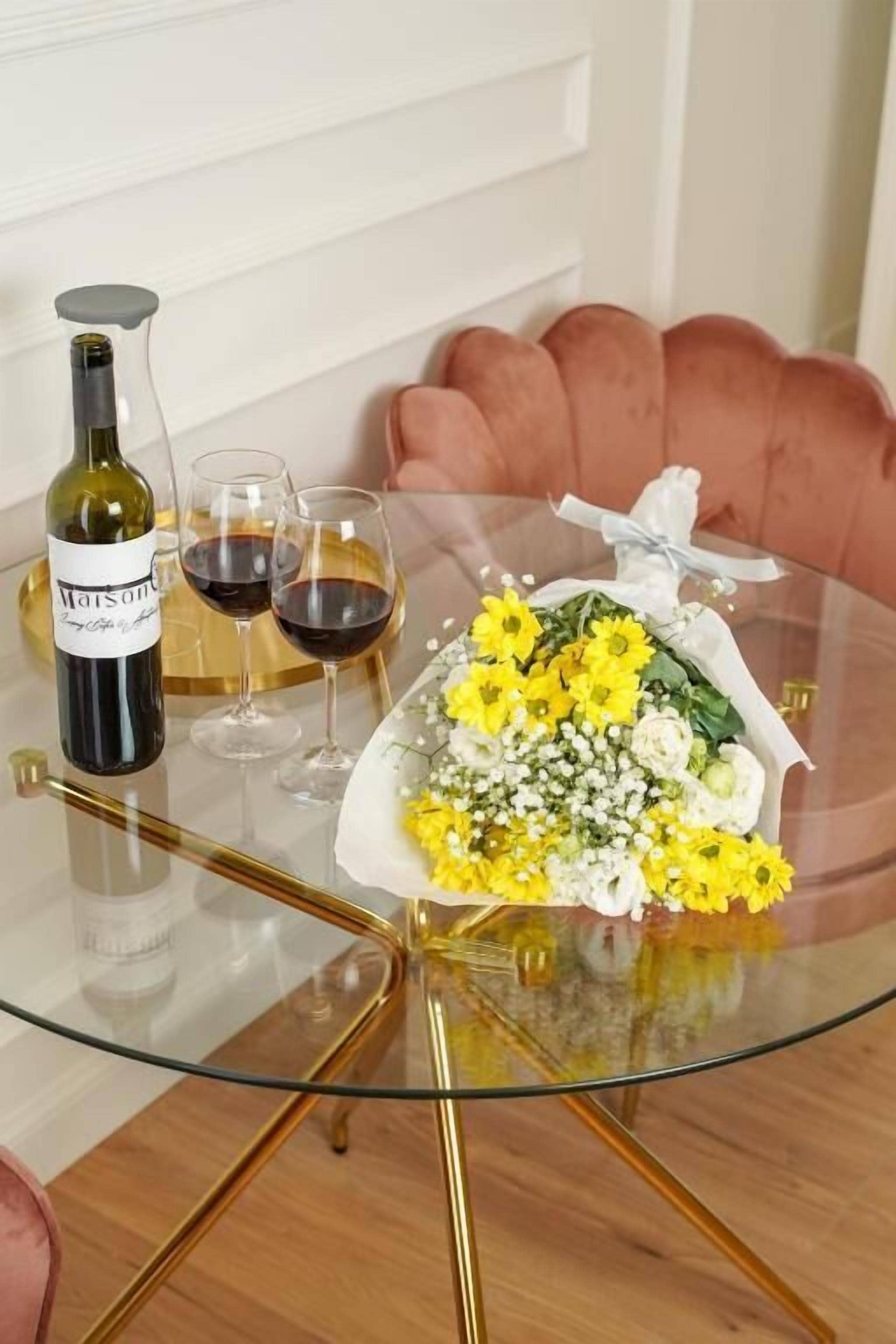 A glass table with a bottle of wine, two wine glasses, and a bouquet of flowers.
