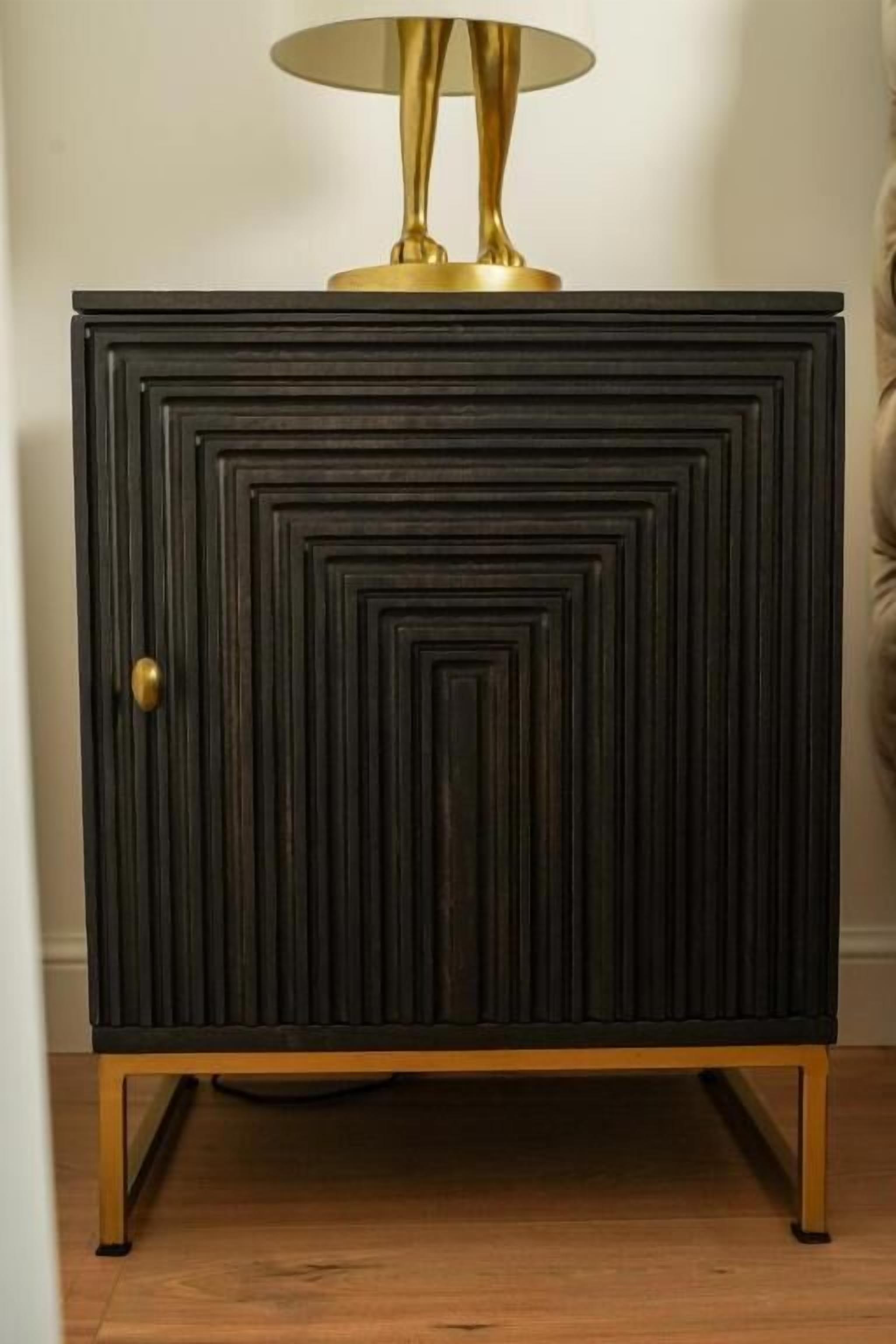 Een donkere houten kast met een messing lamp erop, een messing handgreep en een gouden voet.