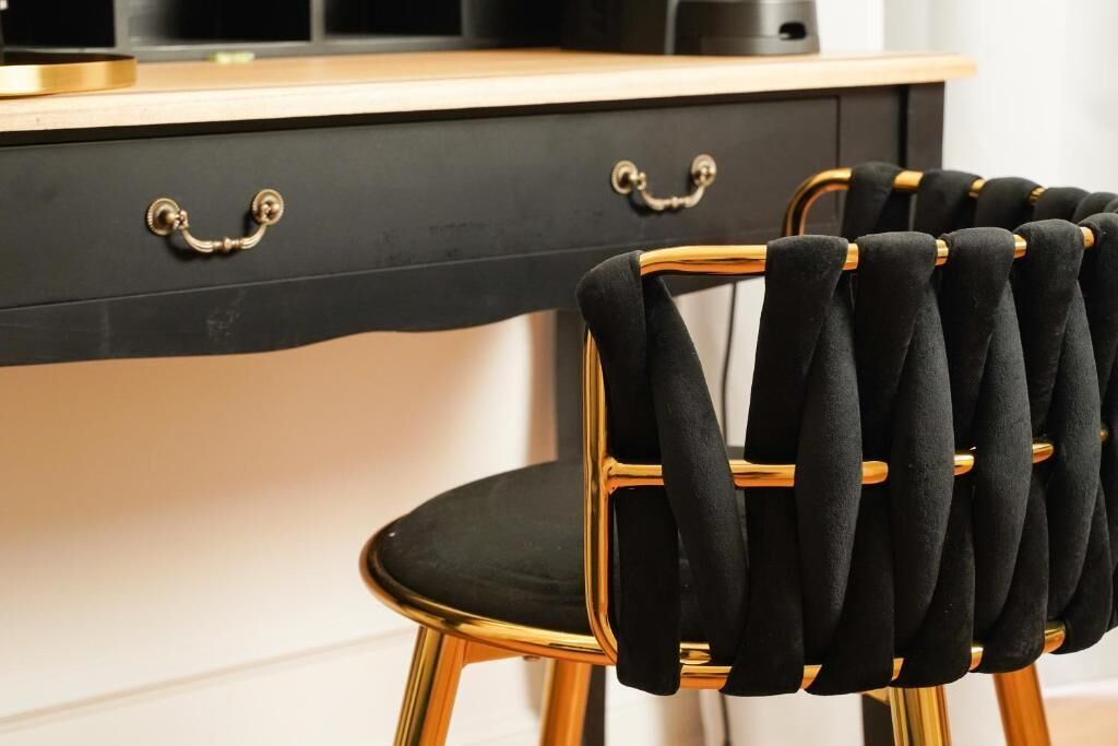A chair with a black upholstered seat and backrest, and gold metal frame, positioned in front of a black cabinet with gold handles.