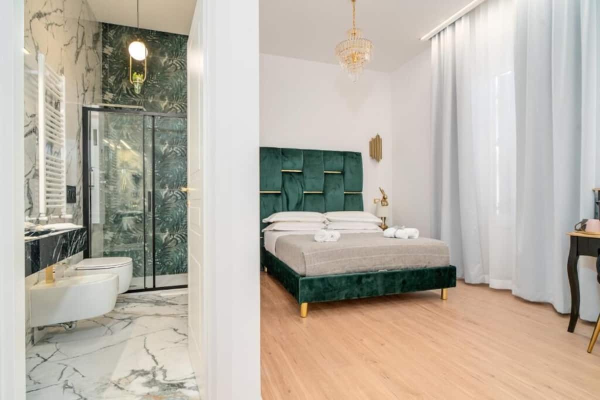 Un dormitorio moderno con un cabecero tapizado en verde, suelo de madera y cabina de ducha de vidrio.