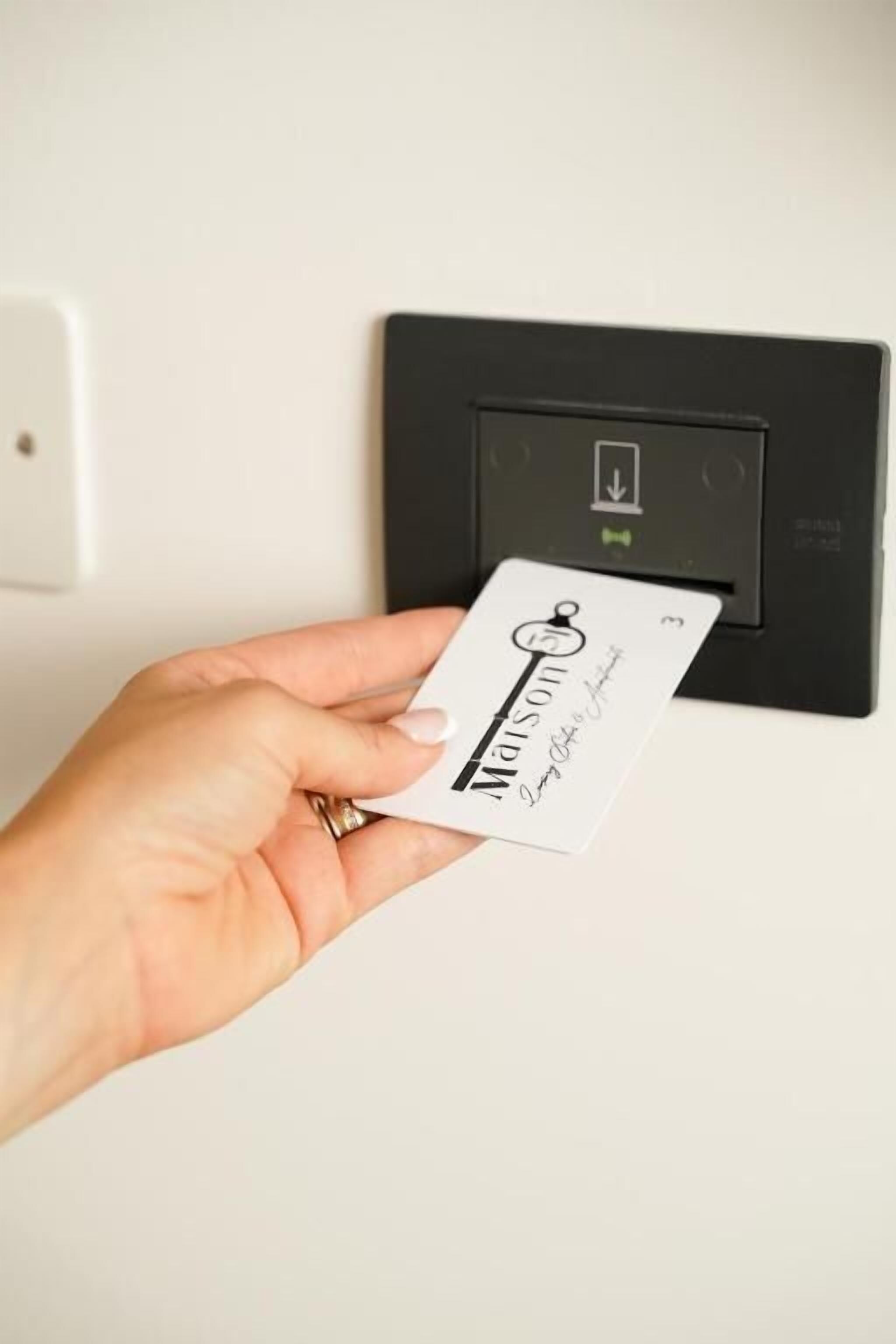 Una mano sostiene una tarjeta con un ojo de cerradura y texto, frente a un dispositivo negro con una luz indicadora verde.