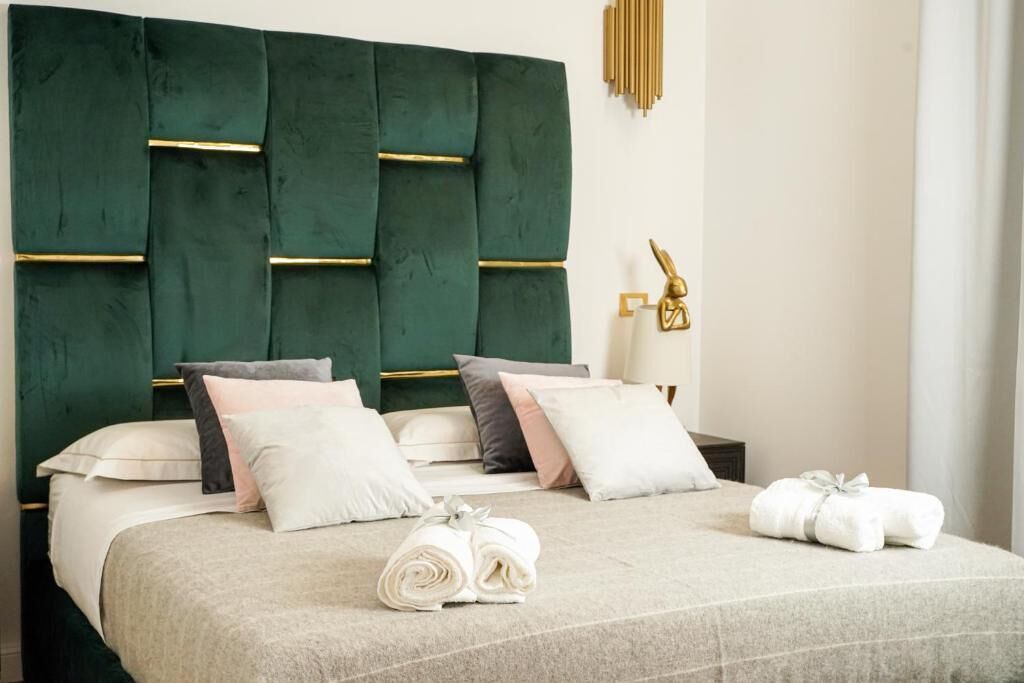 Una cama bien hecha con un cabecero tapizado en verde, varios almohadones y toallas enrolladas sobre la cama.