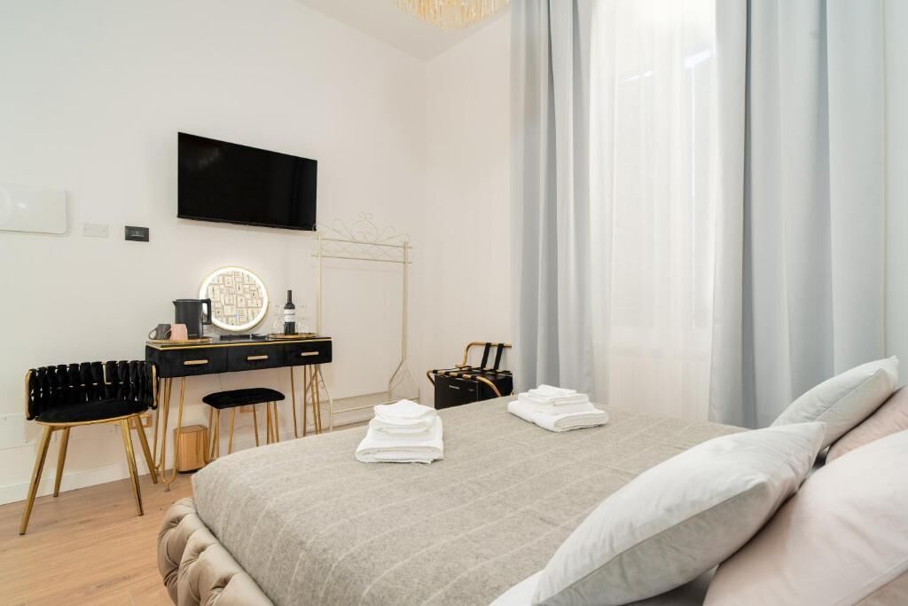 Ein modernes Hotelzimmer mit einem Bett, einem Schreibtisch mit Spiegel, einem Sessel und einem an der Wand befestigten Fernseher.
