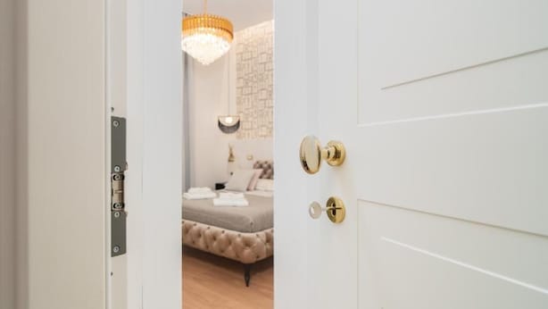 Een slaapkamer met een gebonden bed, een kroonluchter en een witte deur met een gouden handvat.