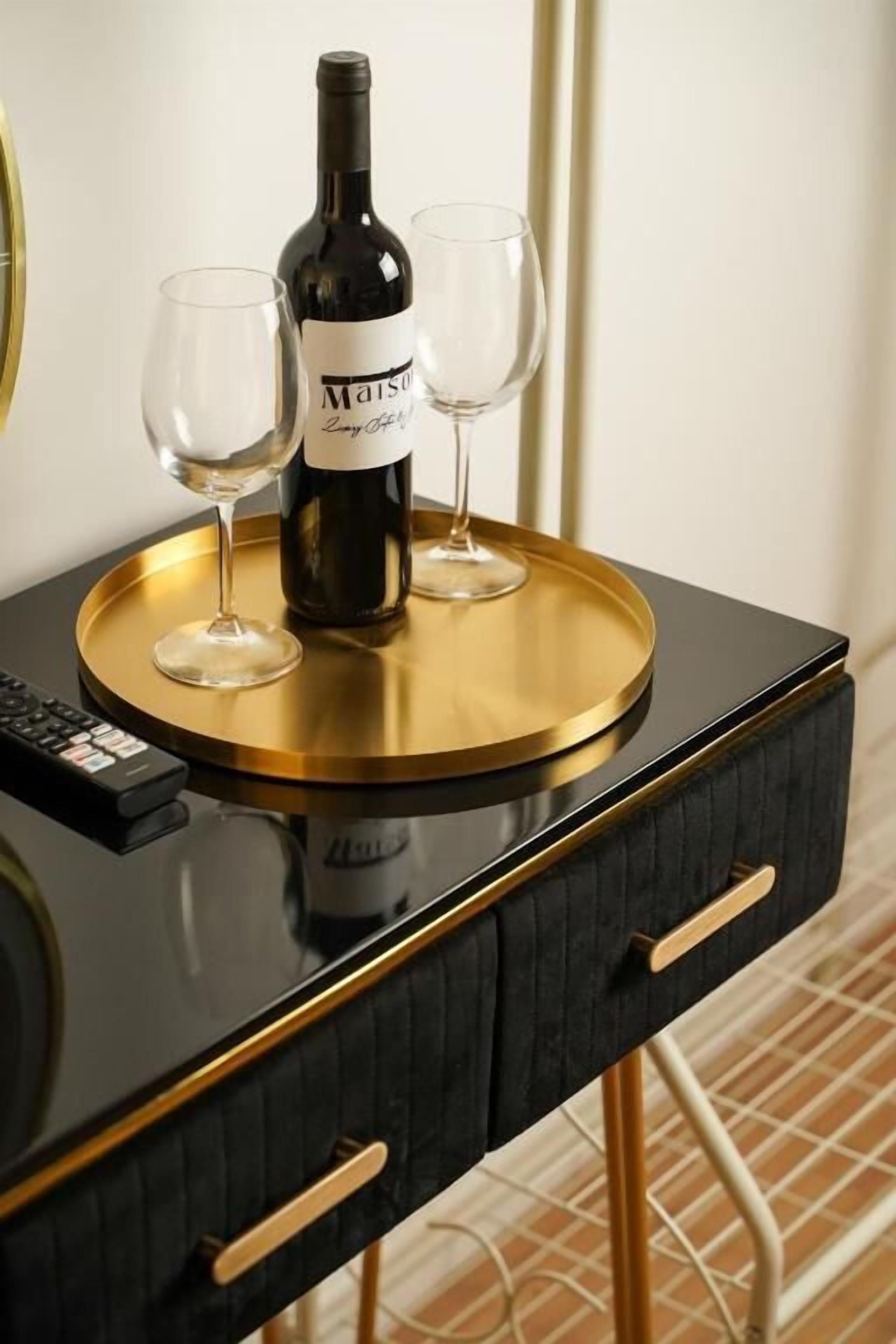 A black and gold side table with a bottle of wine and two glasses on it.