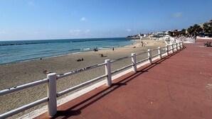 Een boulevard aan zee met een verharde promenade, een strand en een heldere lucht.