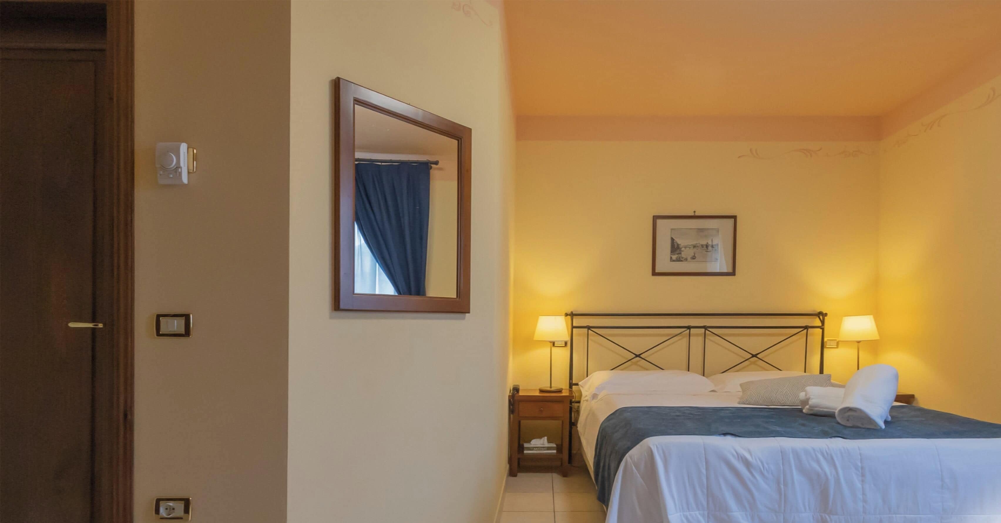 Une chambre d’hôtel avec un lit, des lampes de chevet, une table de chevet, un miroir et un tableau encadré au mur.
