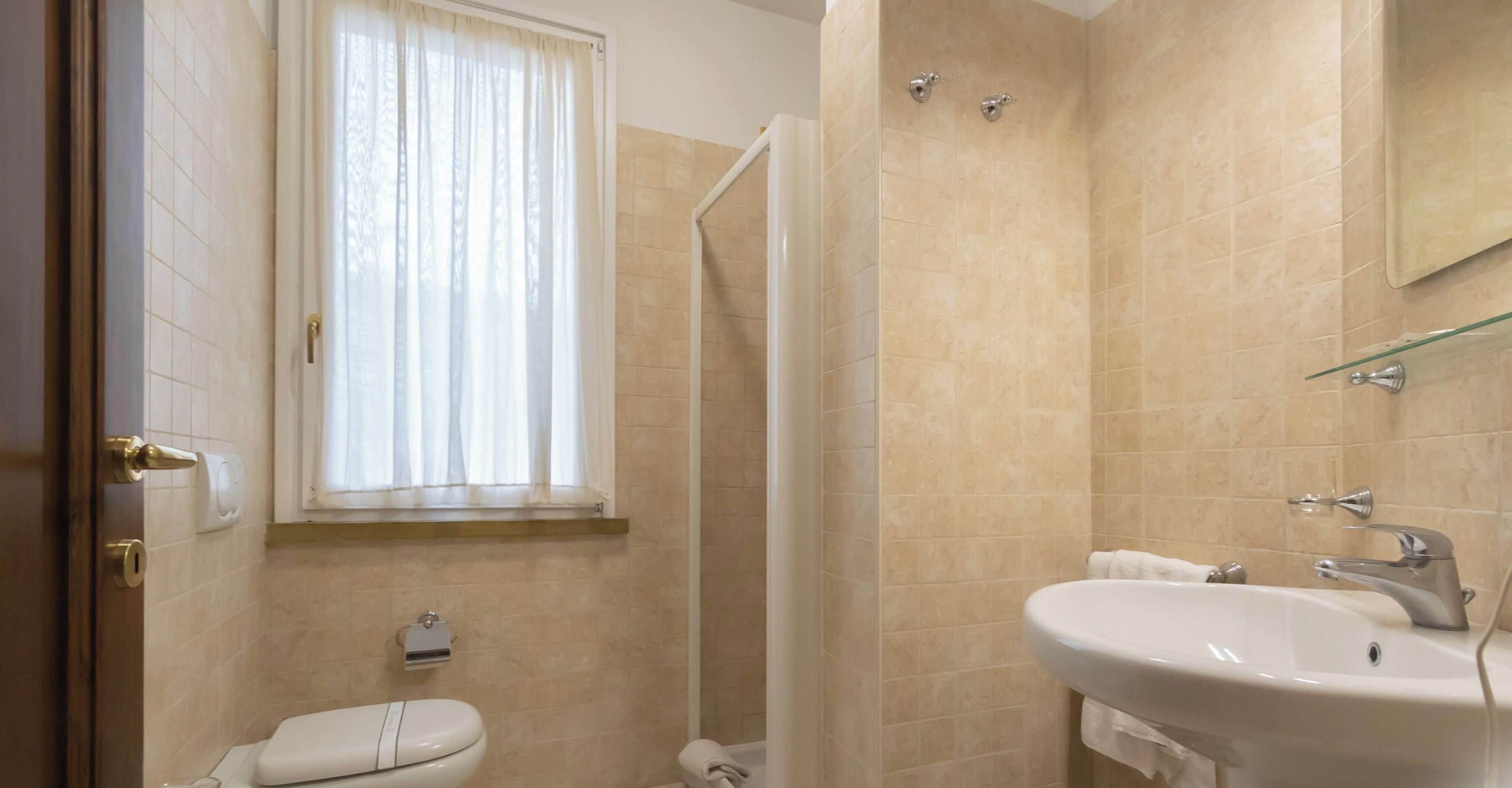 Une salle de bain comprenant des toilettes, un lavabo, une douche et une fenêtre avec des rideaux.
