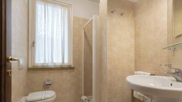 Une salle de bain comprenant des toilettes, un lavabo, une douche et une fenêtre avec des rideaux.