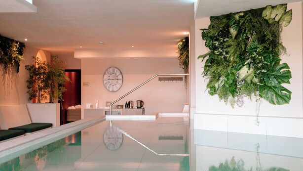 A modern indoor pool area with a clear glass floor, a staircase, and a wall adorned with lush green plants. - Hotiday Toscana Riparbella (Riparbella)