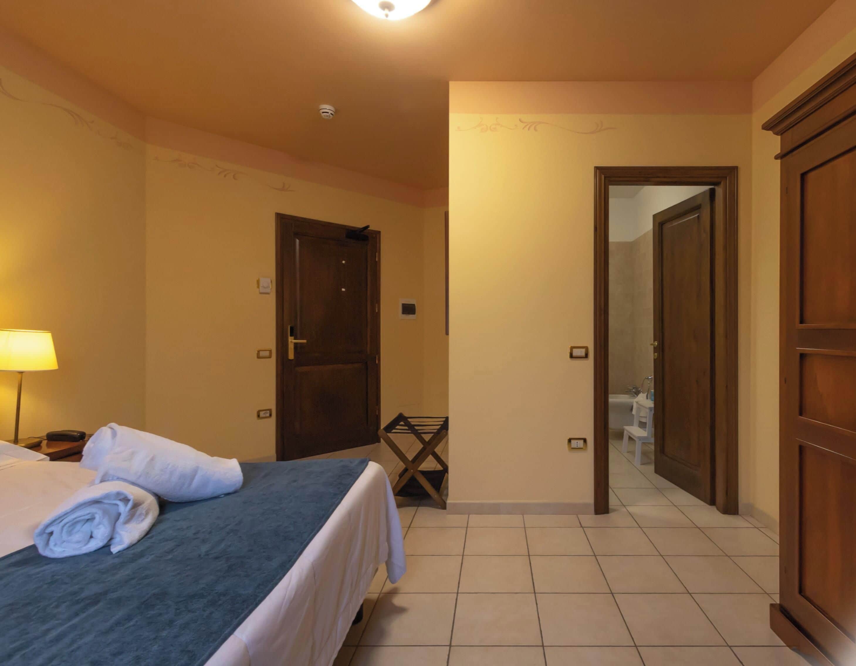 Una habitación de hotel con cama, una silla, escritorio con lámpara y armario.