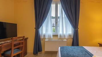 Una camera d'albergo con un letto, una scrivania con una sedia, una televisione e una finestra con tende.