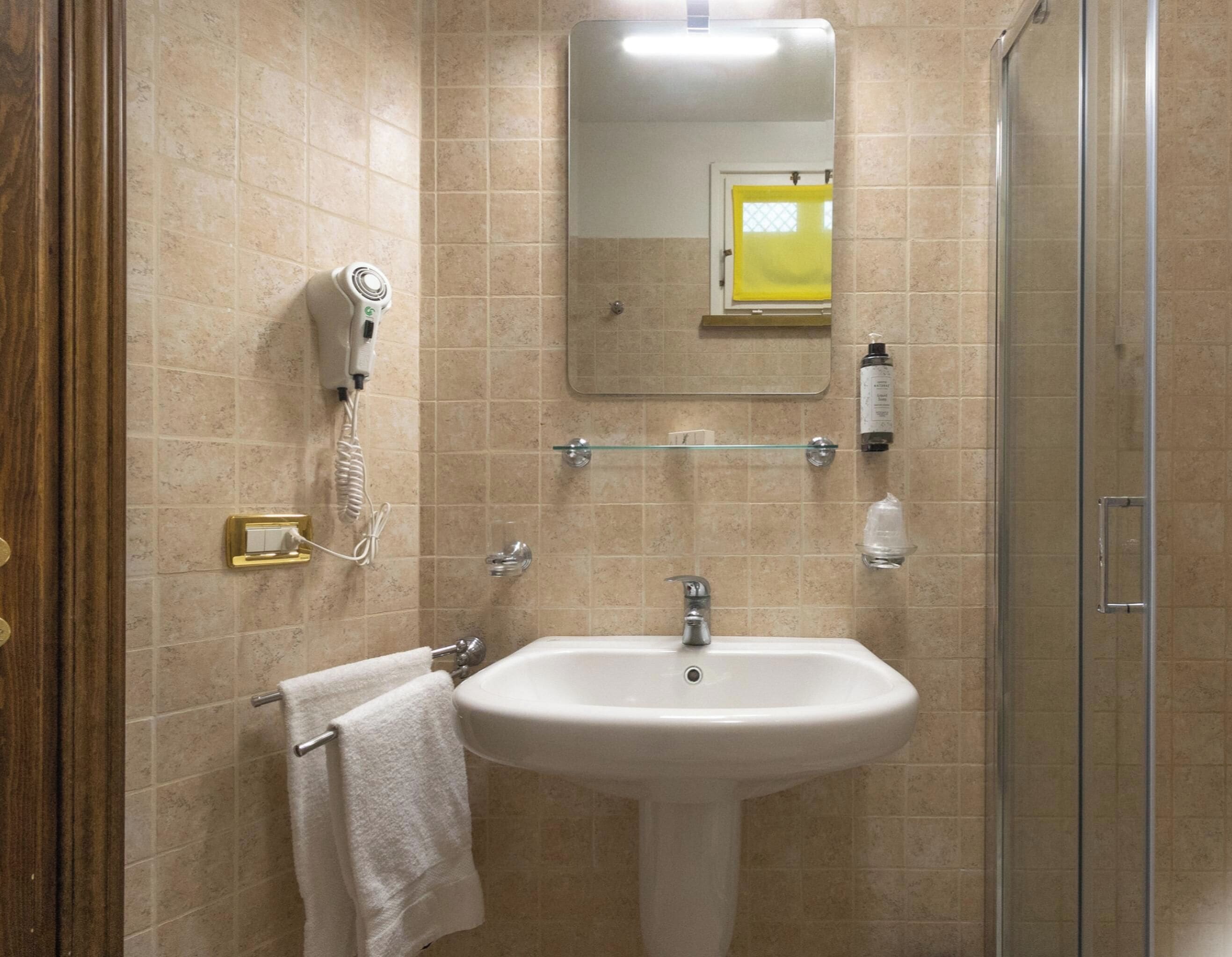 Une salle de bain avec un lavabo blanc, un miroir, un sèche-cheveux et une cabine de douche en verre.