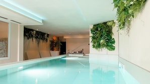 A modern indoor swimming pool with a clear, reflective surface, surrounded by walls adorned with lush green plants. - Hotiday Toscana Riparbella (Riparbella)