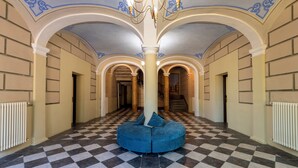 A spacious hallway with a checkered floor, a central blue seating area, and a staircase in the background. - Hotiday Toscana Riparbella (Riparbella)