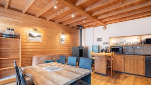 Un interior de madera con una mesa de comedor, sillas, una zona de cocina y vigas de madera en el techo.