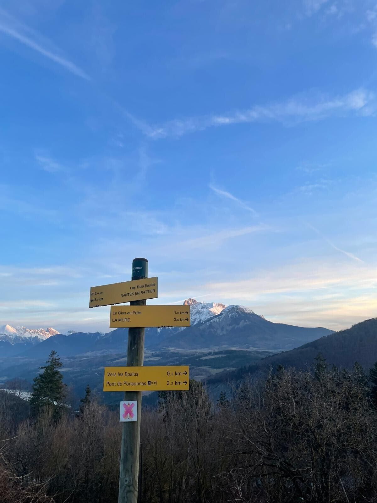 Un panneau indicateur directionnel avec plusieurs panneaux indiquant différentes destinations, le tout sur fond de paysage montagneux.