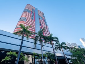 A tall hotel with a curved facade, multiple balconies, and palm trees in front.