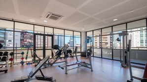 A gym with exercise equipment, large windows, and a view of buildings. - Units at Salvador Boulevard Hotel - Msbs (Salvador)