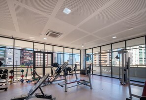 A gym with exercise equipment, large windows, and a view of buildings.