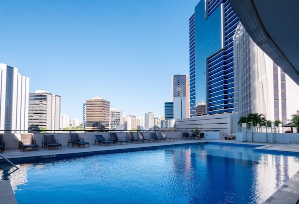 A rooftop pool with lounge chairs, surrounded by high-rise buildings.