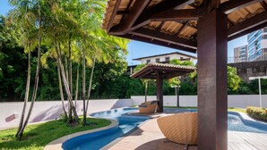 A pool area with a pergola, palm trees, and a building in the background. - Units at Salvador Boulevard Hotel - Msbs (Salvador)