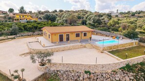 Uma casa amarela de dois andares com piscina e muros de pedra.