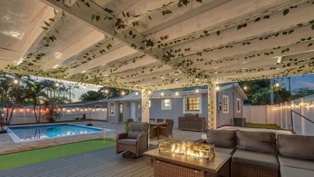 Une terrasse extérieure avec une piscine, des meubles en osier et des guirlandes lumineuses.