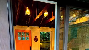 A room with a wooden ceiling, a bed with a green bedspread, a window with a view of trees, and a door with a red handle. - The Roost - A Pet Friendly, Creekside Mountain Cabin in the Heart of Adventure! (Collettsville)