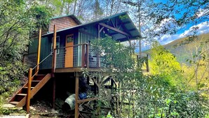 A wooden cabin with a balcony, surrounded by trees and a mountain backdrop. - The Roost - A Pet Friendly, Creekside Mountain Cabin in the Heart of Adventure! (Collettsville)