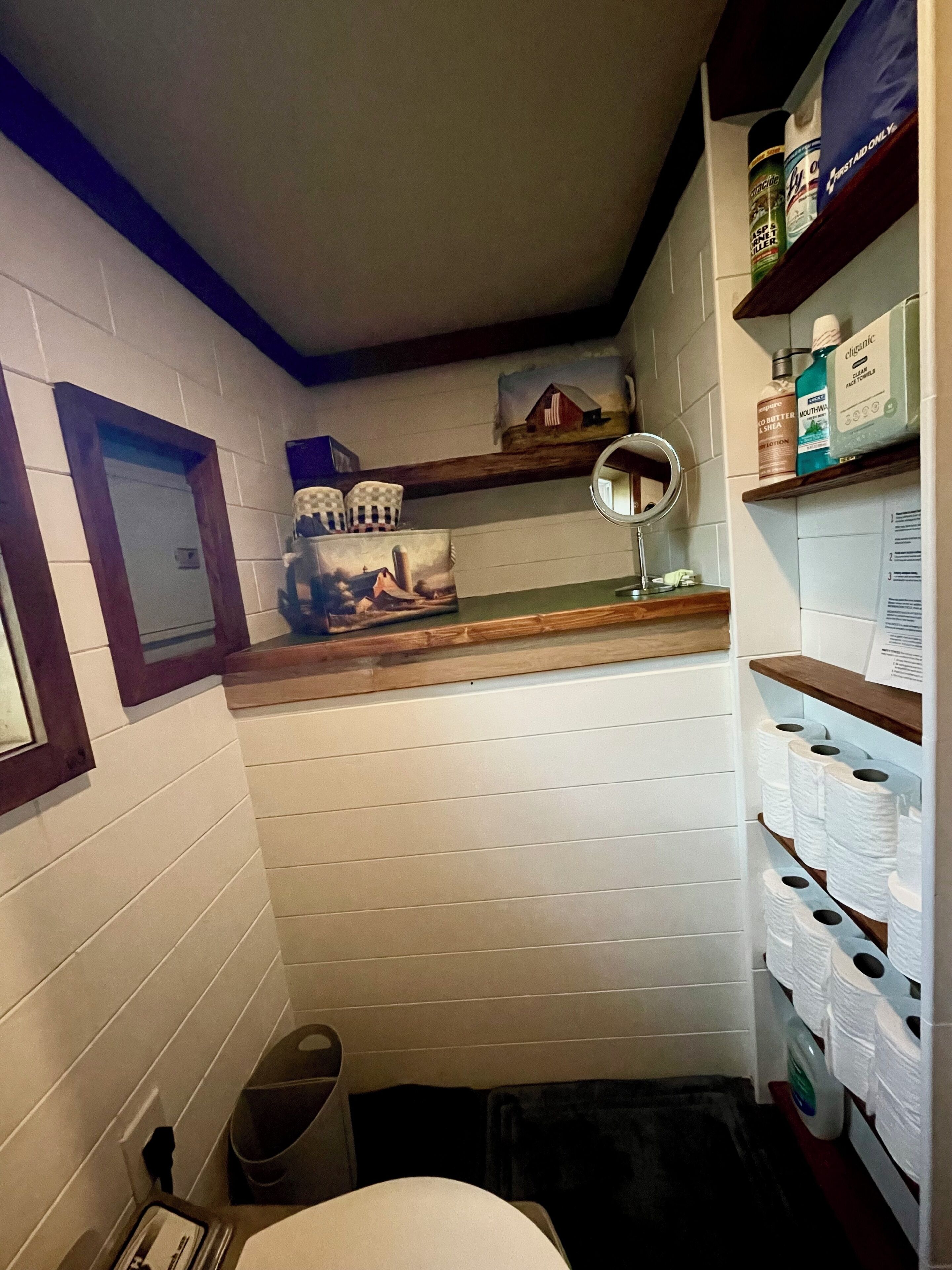 A compact bathroom with a toilet, sink, and shelves with toiletries.