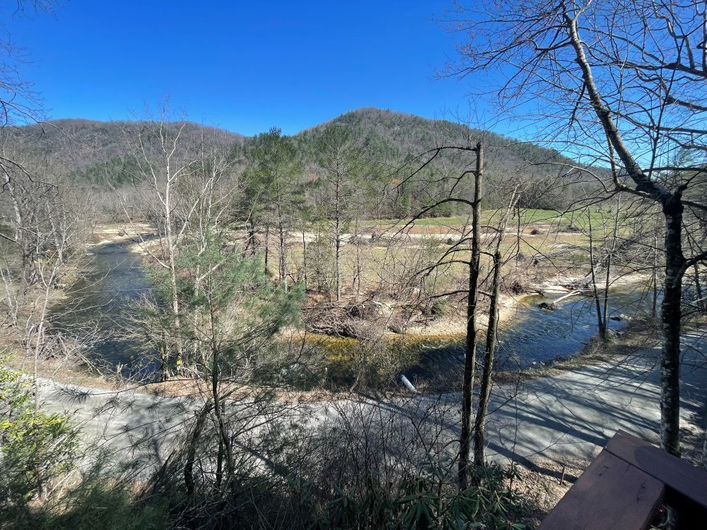 A natural landscape with a river, trees, and a hilly background.
