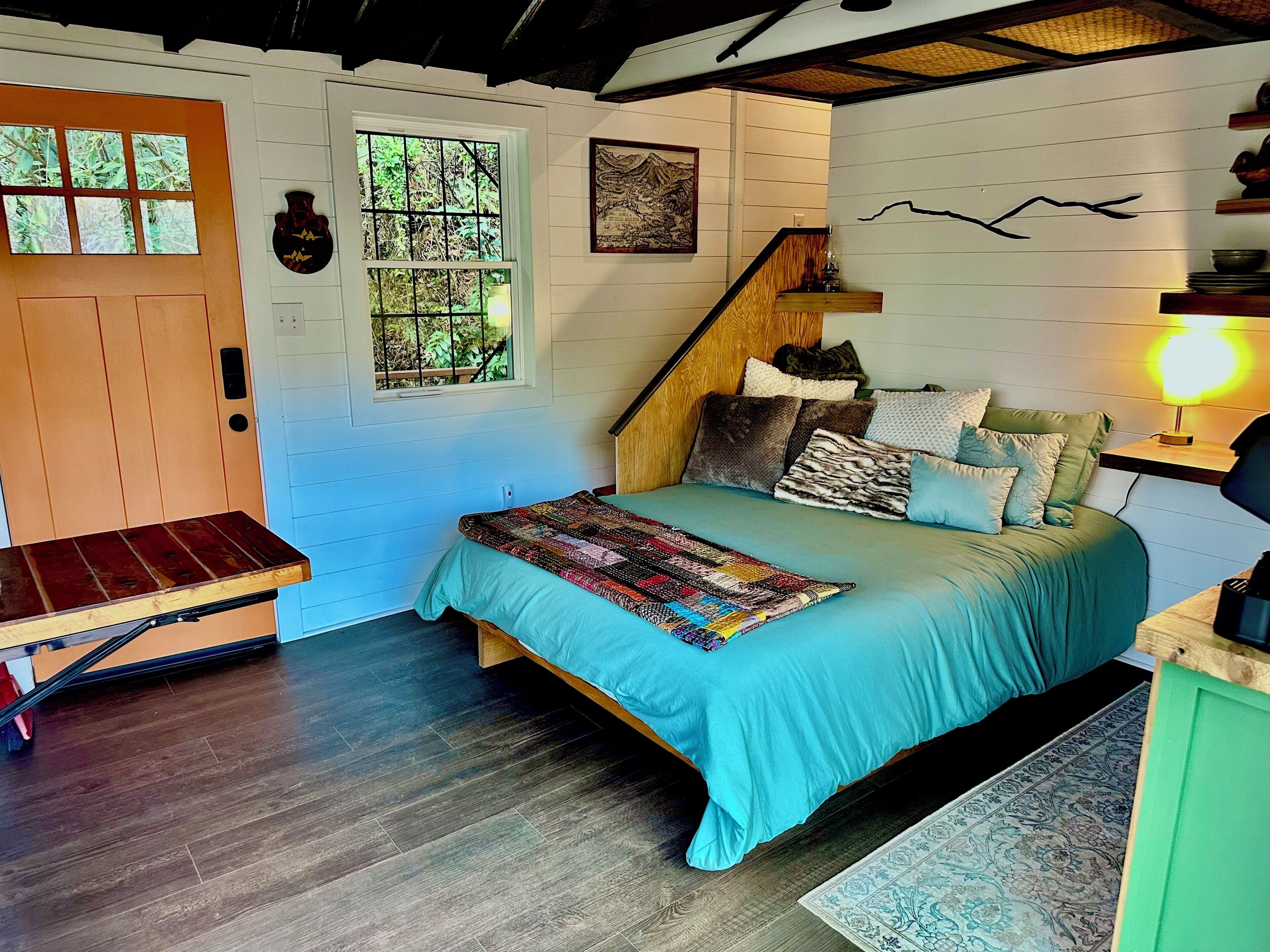 A bedroom with a bed, a wooden bench, a staircase, and a wall-mounted lamp.