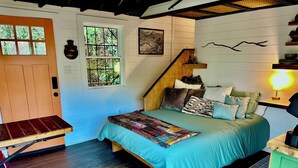 A bedroom with a bed, a wooden bench, a staircase, and a wall-mounted lamp. - The Roost - A Pet Friendly, Creekside Mountain Cabin in the Heart of Adventure! (Collettsville)