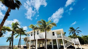 A beachfront house with a balcony, palm trees, and a clear blue sky. - Slipstream 2.0 - A Modern Beachfront Escape (Long Island)