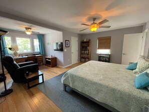 Ein Schlafzimmer mit einem großen Bett, einem Schreibtisch mit Stuhl, einem Bücherregal und einem Deckenventilator.