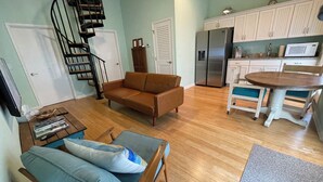 A living room with a sofa, a dining table, a kitchen with cabinets and appliances, and a spiral staircase. - Spacious 5-bedroom "double house" in amazing Santa Rosa Beach with heated pool (Santa Rosa Beach)