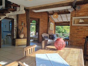 A rustic dining area with a wooden table, chairs, and a red vase. - Casa Perequê (Ilhabela)