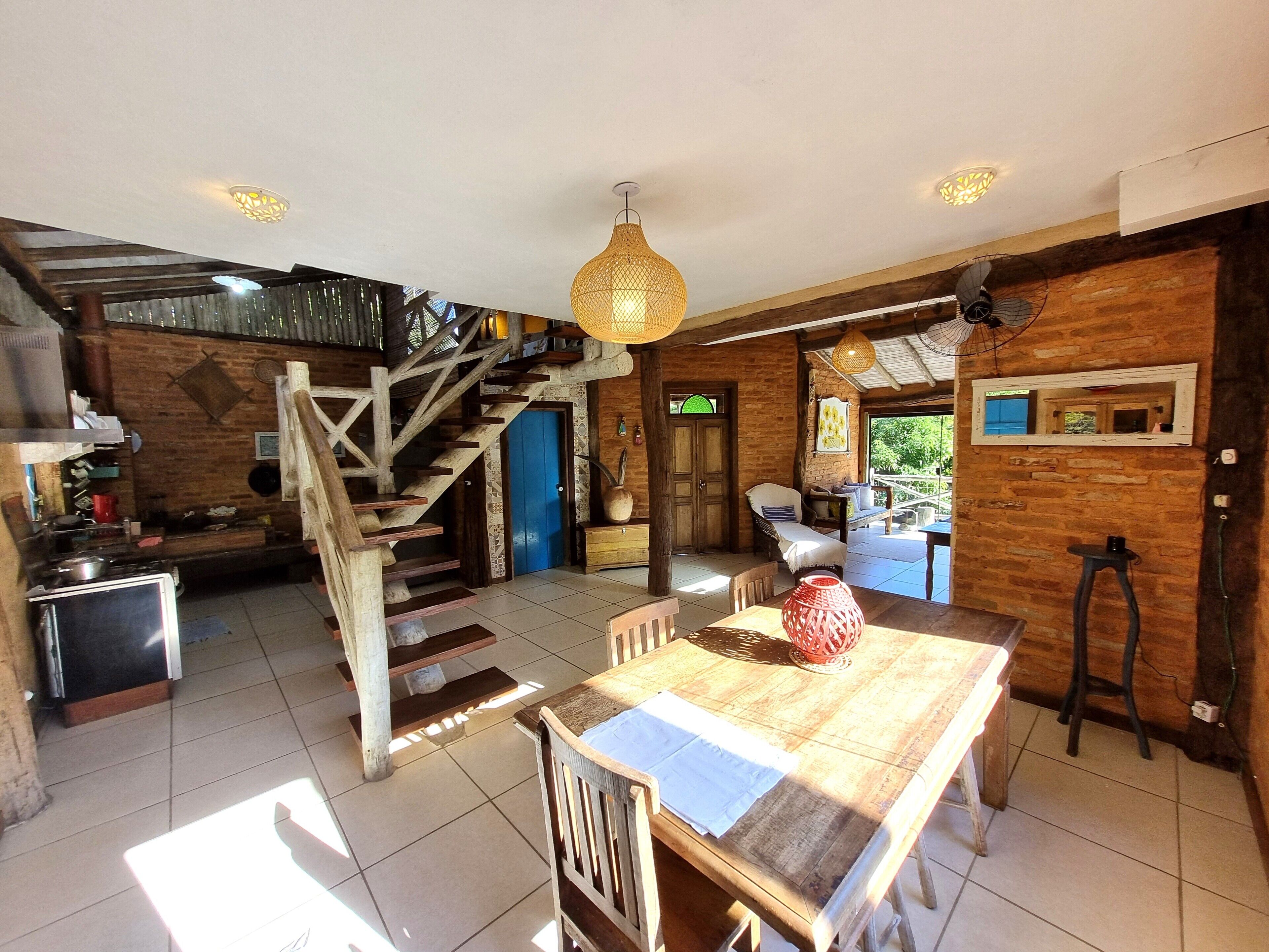 A spacious kitchen with a wooden staircase, a dining area with a large table, and a cozy seating area with a blue door.