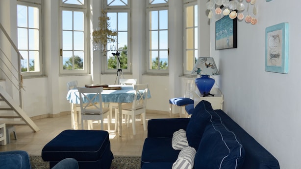 Ein geräumiges Wohnzimmer mit einem blauen Sofa, einem Esstisch mit Stühlen und einer Treppe.