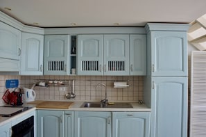 A kitchen with light blue cabinets, a wooden countertop, a sink, and a dish rack.